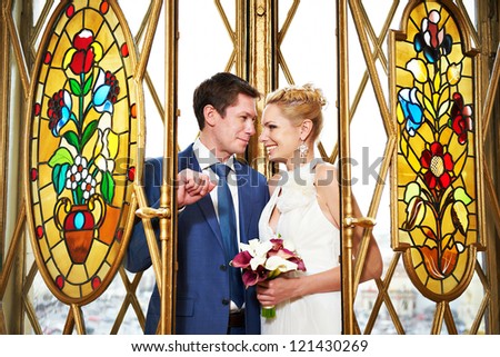 Bride and groom stand near beautiful colorful stained glass windows