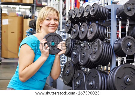 Happy woman chooses loads for dumbbell in the sports shop