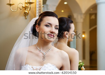Happy beautiful bride near mirror in wedding palace