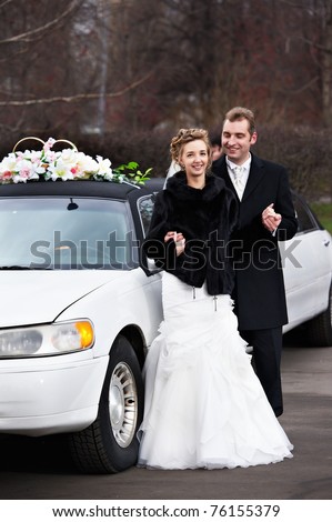 Happy bride and groom near wedding limousine in park