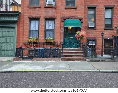 Brownstone Home with Green Awning Pink Petunias and Trash Cans lined up behind rod iron fence in Brooklyn New York USA