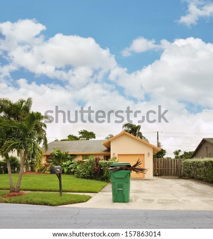 Green Trash container filled with debris suburban home driveway blue sky clouds residential neighborhood USA