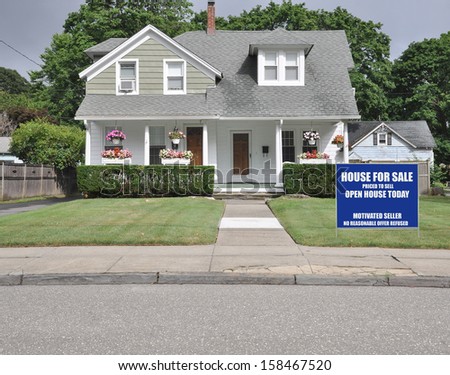Blue For Sale Real Estate Sign on Front yard Lawn of Suburban Cape Cod Style Home Residential Neighborhood USA