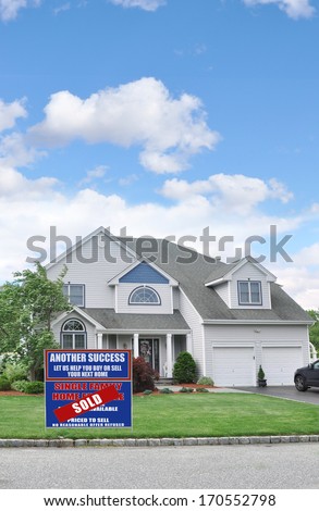 Real Estate Sold (Another Success let us help you buy sell your next home) sign front yard lawn Suburban McMansion style home Residential Neighborhood USA Blue Sky Clouds