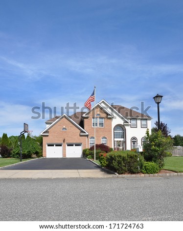 American Flag pole front yard lawn of Suburban McMansion style brick home Landscaped sunny residential neighborhood USA blue sky clouds