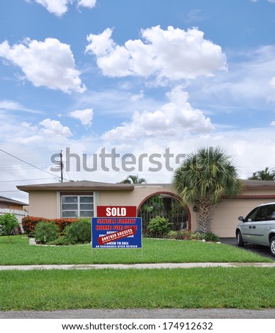 Sold real estate sign \'Another Success Let Us help you buy / sell your next home\' front yard lawn suburban ranch style home residential neighborhood usa blue sky clouds