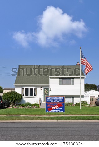 American Flag Pole Sold Real Estate Sign front yard lawn of suburban home residential neighborhood USA blue sky clouds