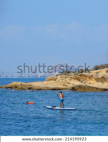 Man paddling on surf board Alicante skyline in distant background Spain Costa Blanca Europe