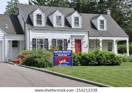 Sold Real Estate (Another Success let Us Help you Buy Sell your Next Home) Sign on front yard lawn of Suburban Cape Cod Colonial Style Home Sunny Residential Neighborhood USA