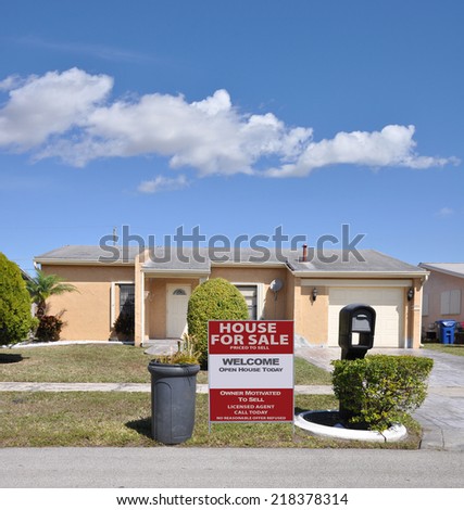 For Sale Real Estate sign on front yard lawn suburban ranch style home with trash can on curb side residential neighborhood USA blue sky clouds