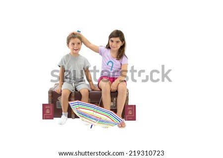 Siblings (boy silly face, girl looking at camera) sitting on vintage luggage with european union spain passports and umbrella isolated on white background