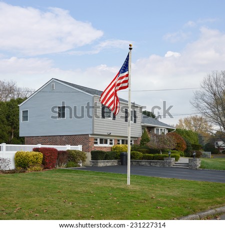 American flag pole suburban high ranch style home autumn season residential neighborhood blue sky clouds USA