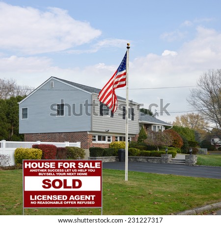 American flag pole real estate sold (another success let us help you buy sell your next home) on lawn of suburban high ranch style home autumn season residential neighborhood blue sky clouds USA