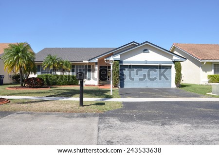 Suburban back split style home black mailbox two car garage palm trees residential neighborhood clear blue sky USA