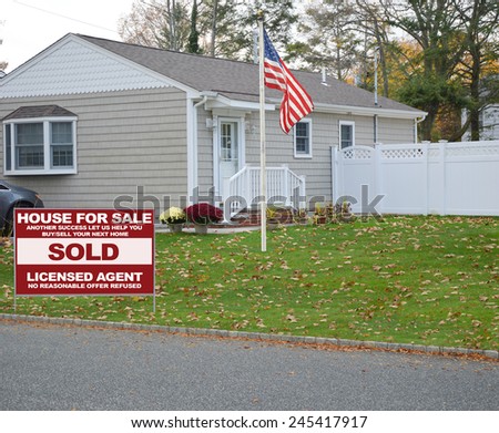 American flag pole sold real estate (another success let us help you buy sell your next home) sign Tan bungalow style home bay window residential neighborhood autumn day mums flowers overcast day USA