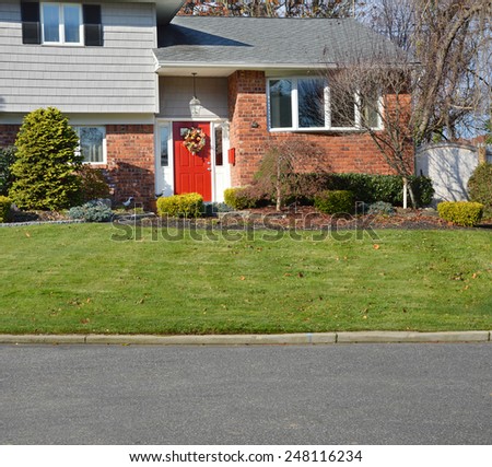 Suburban brick high ranch home with red door, landscaped yard, sunny residential neighborhood USA