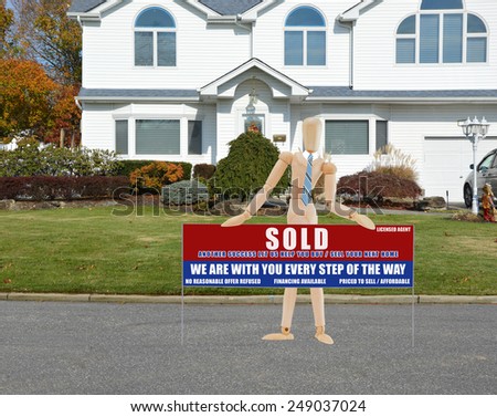 Mannequin wearing blue striped tie holding Real estate sold (another success let us help you buy sell your next home) sign closeup of suburban mcmansion autumn day residential neighborhood USA