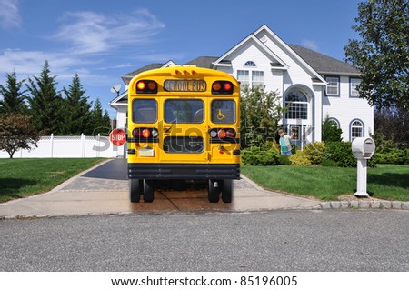 Little Boy Happy School Bus with Stop Sign Extended is Parked in Driveway of Luxury Suburban Home Sunny Day