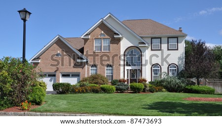Suburban Brick Siding Two Car Garage Home Landscaped Front Yard in Residential District on Blue Sky Day