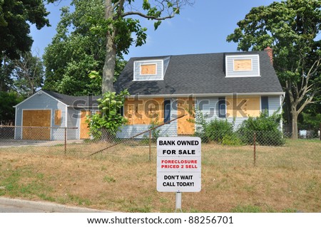 Bank Owned Foreclosure For Sale Sign on Front Yard Lawn of Cape Code Style Suburban Home in Residential Neighborhood