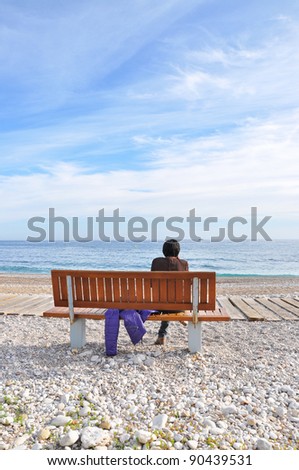 Woman sitting on Wood Bench with back facing camera on a Beach Path in Villa Joyosa Spain a town in the province of Alicante in late afternoon