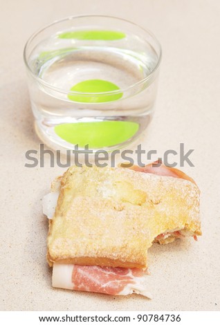 Spanish Mediterranean Jamon Bocadillo missing a bite  (Cured Ham Sandwich) Glass of water in background