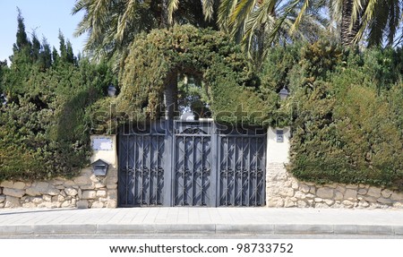 Mediterranean Spanish Style Home Gate Entrance with Landscaped Evergreen Shrubs Palm Trees in the community of Valencia and the province of Alicante Spain Europe