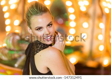 Beautiful young woman in a venue with party lights dressed in a stylish sexy black dress looking back over her shoulder at the camera with a smile