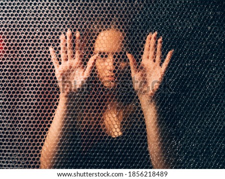 Quarantine self isolation. Pandemic anxiety. Social distancing. Textured art portrait of bored unhappy annoyed trapped woman in black touching plastic bubble wrap wall in darkness. Foto stock © 