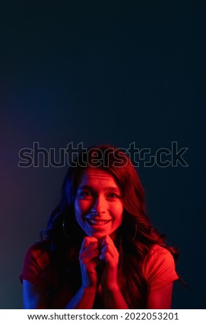 Pleading woman. Asking apology. Request favor. Begging please. Cute smiling young girl with imploring expression in bright red color neon light on dark copy space background. Imagine de stoc © 