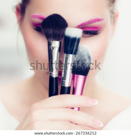 The makeup artist with bright pink make-up holds powder brushes. She covers with them the face. Studio portrait.