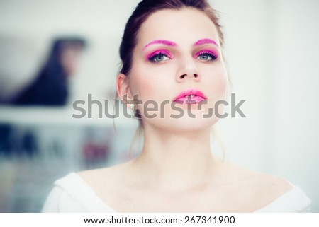 The woman with a bright pink make-up attentively looks forward. Studio portrait.