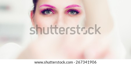 The woman with a bright pink make-up and pink eyebrows hides the face in hands. Studio portrait.