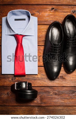 Man\'s collection: a shirt with a bright tie, shoes and a belt on a wooden background