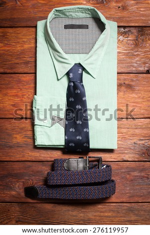 Man\'s collection of clothes in casual style consisting of a men\'s shirt, a tie with a  bicycles print and a belt on a wooden background
