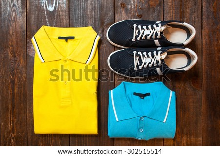Bright men\'s t-shirts (polo) and sports shoes on a dark wooden background of a show-window of shop