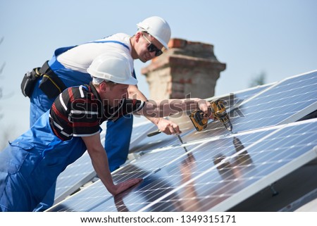 Male team workers installing stand-alone solar photovoltaic panel system using screwdriver. Electricians mounting blue solar module on roof of modern house. Alternative energy sustainable concept Сток-фото © 