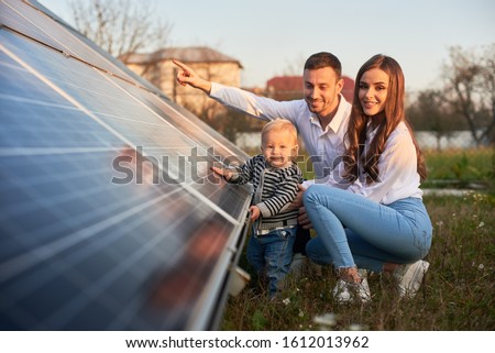 A young family of three is crouching near a photovoltaic solar panel, smiling and looking at the camera, concept of bright future Сток-фото © 