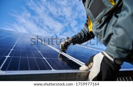 Close up of man technician in work gloves installing stand-alone photovoltaic solar panel system under beautiful blue sky with clouds. Concept of alternative energy and power sustainable resources.