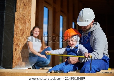 Father, mother and son building wooden frame house. Toddler boy helping his daddy, while woman looking for them on construction site. Guys wearing helmet and blue overalls. Carpentry, family concept. Photo stock © 