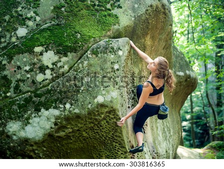Young woman climbing on large boulders outdoor summer day