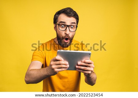 Amazed happy bearded man using digital tablet looking shocked about social media news, astonished man shopper consumer surprised excited by online win isolated over yellow background. Stockfoto © 
