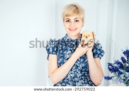 Portrait of a smilling beautiful blonde girl holding skull in a white room