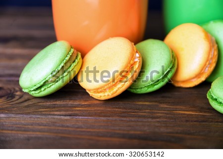 Close view at french pistachios and orange macaroons standing in a row in dark colors on a wooden background with orange cup. Shallow depth of field.