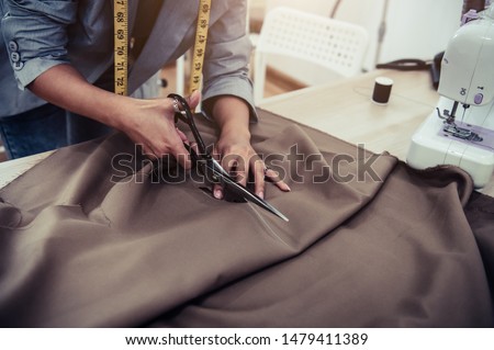 Dressmaker cutting dress fabric on sketch line with sewing machine. Fashion designer tailor or sewer in workshop studio designing new collection clothes. Business owner shop and entrepreneur concept 商業照片 © 