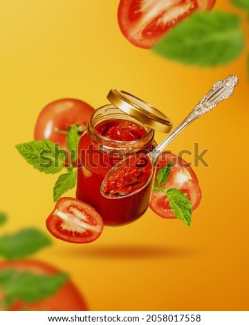 Flying jar with tomato sauce. Jar of tomato sauce, ripe slices of tomato and spoon fly in air. Creative food background.