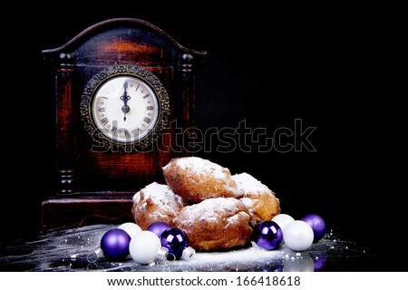Dutch donut also known as oliebollen, traditional New Year\'s eve food, clock on midnight over black background