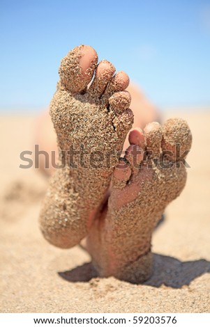 bottom of male feet covered with sand on the beach in sunshine