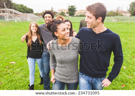 Multiethnic Group of Friends at Park. A caucasian Man with a Mixed-Race Woman are in foreground and some others in background. They seem to be happy