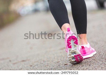 Female Runner Shoes closeup on the road, town setting. Shallow depth of Field, focus on rear shoe.